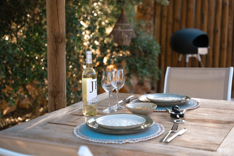 Mesa exterior preparada con vino y platos en Lodge Lua, Portugalvillas - Glamping Algarve, rodeada de naturaleza.