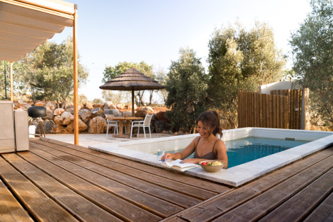 Kvinde slapper af i poolen ved Lodge Lua - Portugalvillas Glamping Algarve med bog og frugt i solskinnet.