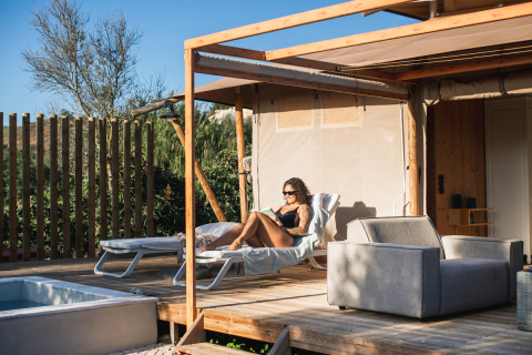 Kvinde slapper af på Lodge Lua, Portugalvillas Glamping Algarve, solrig terrasse med pool og natur.