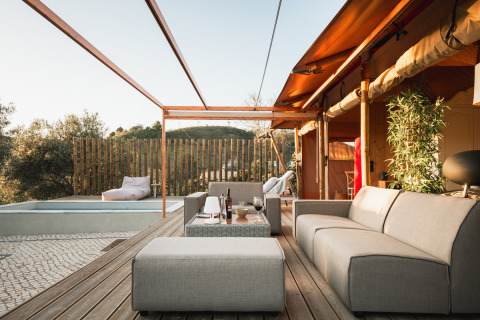 Zona exterior relajante en Lodge Lua, Portugalvillas Glamping Algarve, con sofás, piscina y vistas verdes.