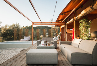 Zona exterior relajante en Lodge Lua, Portugalvillas Glamping Algarve, con sofás, piscina y vistas verdes.