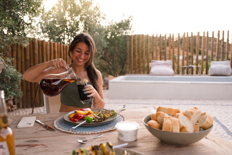 Kvinde nyder udendørs middag ved since Lodge Lua, Glamping Algarve, Portugal, med brød og drikkevarer.