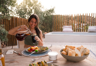 Kvinde nyder udendørs middag ved since Lodge Lua, Glamping Algarve, Portugal, med brød og drikkevarer.