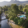 Aerial view of Huttopia Millau - Glamping Aveyron featuring a pool, river, and lush green mountain scenery.