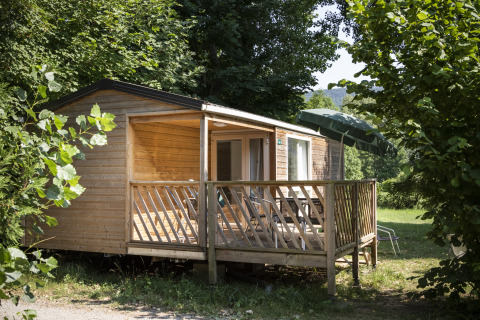 Alojamiento glamping en cabaña de madera en Huttopia Millau - Glamping Aveyron, rodeado de naturaleza verde.