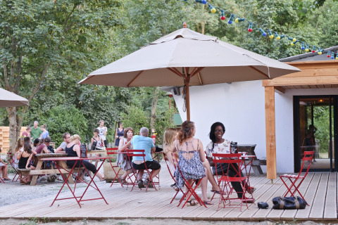 Udendørs glampingområde hos Huttopia Millau - Glamping Aveyron med gæster, parasoller og lyskæder.