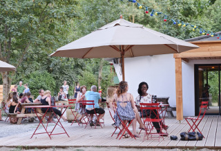 Zona de estar al aire libre en Huttopia Millau - Glamping Aveyron con huéspedes, sombrillas y guirnaldas de luces.