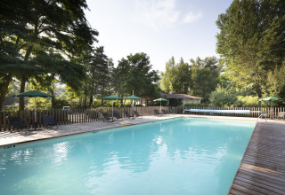 Outdoor swimming pool with wooden deck, sun loungers, and umbrellas at Huttopia Millau - Glamping Aveyron in nature.
