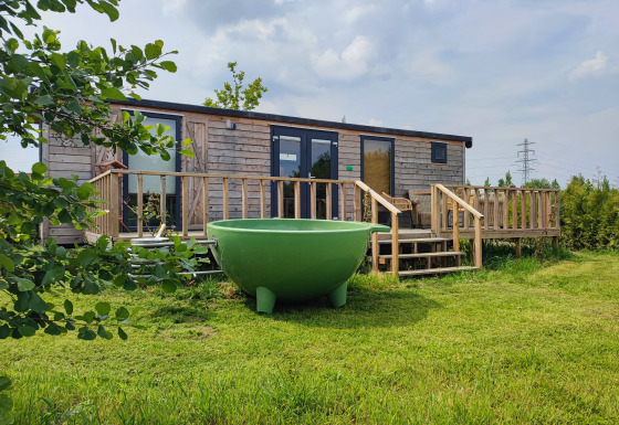 Glamping-Unterkunft bei Stadslandgoed De Heicohoeve in Gelderland, Niederlande, mit Holzwohnwagen und grünem Außenbad.
