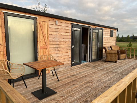 Terraza de madera con sillas en alojamiento glamping Stadslandgoed De Heicohoeve - Pipowagens Gelderland en la naturaleza.