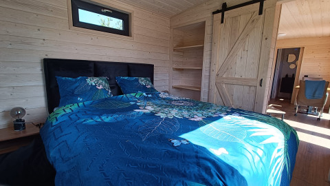 Et komfortabelt soveværelse med dobbeltseng, blåt sengetøj og træinteriør i en glamping-indkvartering.
