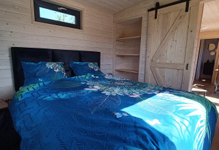 Camera accogliente con letto matrimoniale, biancheria blu e interni in legno in glamping a Gelderland.