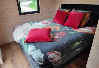 Knus bed met bloemendeken en rode kussens in glamping Stadslandgoed De Heicohoeve Pipowagens Gelderland.