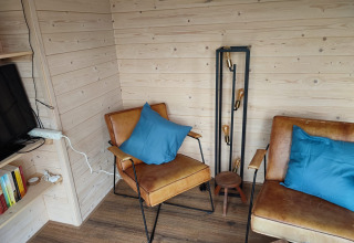 Hyggeligt glampinghjørne på Stadslandgoed De Heicohoeve med brune lænestole, blå puder og retrolampe.