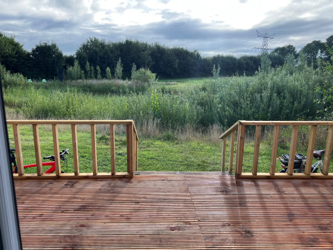 View from wooden terrace across meadow and trees at Stadslandgoed De Heicohoeve - Pipowagens Gelderland.