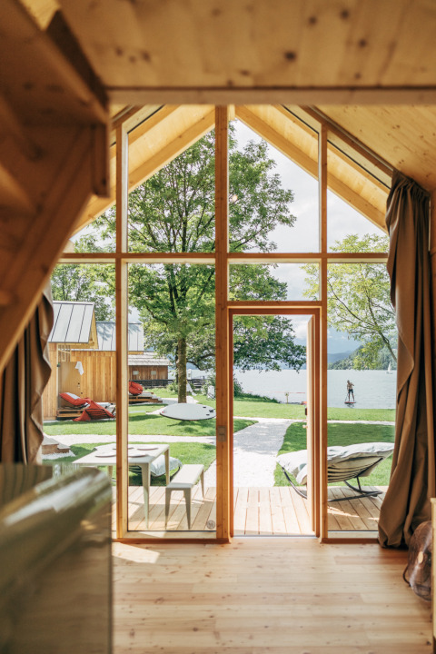 Interior view from Eco Lodges Millstätter See, looking over lawn, lake and paddle boarder in Austria.