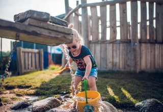 Kind speelt met water en zand bij een houten speeltoestel in vakantiepark Ackersate, Gelderland, Nederland.