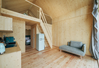 Innenansicht einer modernen Holzhütte mit Schlafempore, Küchenzeile, Retro-Kühlschrank und Sofa in Eco Lodges Millstätter See.