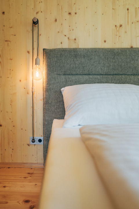 Moderne glampingindkvartering på Eco Lodges Millstätter See med trævæg, seng og hængende pære.