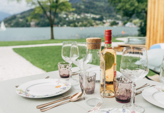 Mesa al aire libre con vino, copas y platos en Eco Lodges Millstätter See junto al lago en Austria.