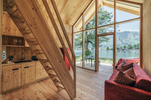 Binnenzicht van Eco Lodges Millstätter See in Oostenrijk met houten interieur, glaswand en zicht op het meer.