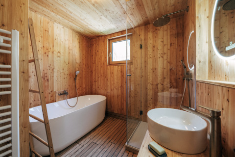 Baño de madera moderno con bañera, ducha y lavabo en Eco Lodges Millstätter See, alojamiento glamping.