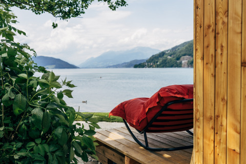 Udsigt over søen fra en træhytte ved Eco Lodges Millstätter See med en rød liggestol på terrassen.