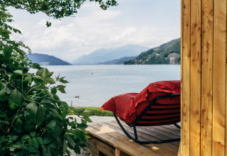 Zicht vanuit een houten lodge bij Eco Lodges Millstätter See met een rood ligbed en het meer op de achtergrond.