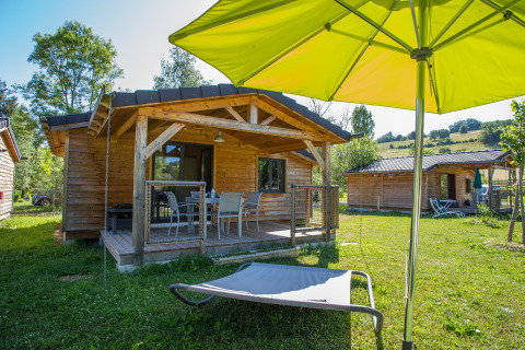 Gemütliche Holzchalets beim Glamping auf Camping Détente et Clapotis, Auvergne-Rhône-Alpes, mit Terrasse und Sonnenschirm.