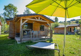 Houten glampingverblijf bij Camping Détente et Clapotis, Auvergne-Rhône-Alpes, met ligstoel en terras.