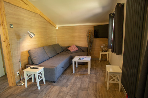 Glamping living area at Camping Détente et Clapotis with gray sofa, TV, and wooden decor, Rhône-Alpes.