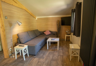 Salon glamping au Camping Détente et Clapotis avec canapé gris, TV et décoration bois en Rhône-Alpes.