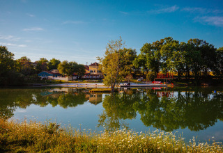 Whaka Lodge glamping al lado de un lago en el sur de Francia, rodeado de árboles, flores y agua reflejada.