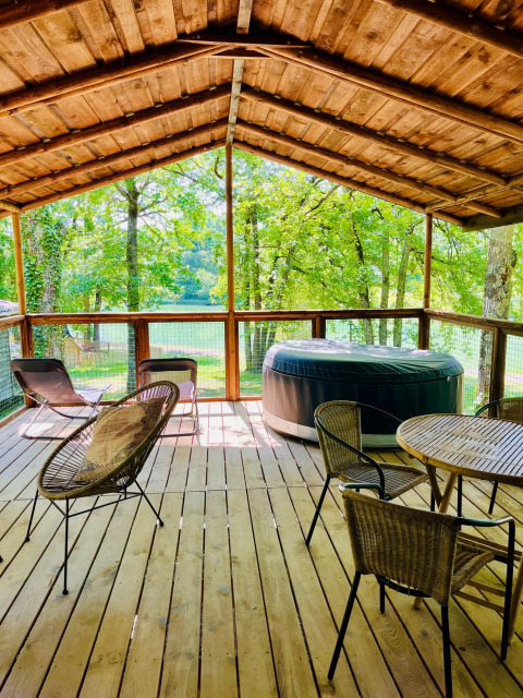 Terraza de madera con jacuzzi y sillas en Whaka Lodge glamping, rodeada de naturaleza en el sur de Francia.