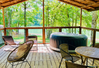 Houten veranda met bubbelbad en zitje bij Whaka Lodge glamping, omringd door natuur in Zuid-Frankrijk.