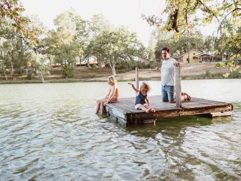 Family enjoys relaxing on a wooden dock by the lake at Whaka Lodge Glamping, South France nature camp.