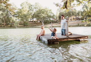 Famiglia si rilassa su un pontile in legno al lago presso Whaka Lodge Glamping, campeggio natura in Francia.