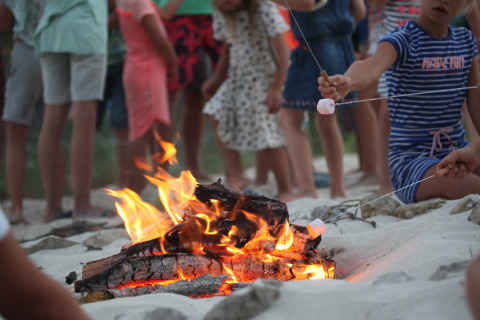 Kinderen roosteren marshmallows bij het kampvuur op het strand bij Whaka Lodge Glamping in Zuid-Frankrijk.