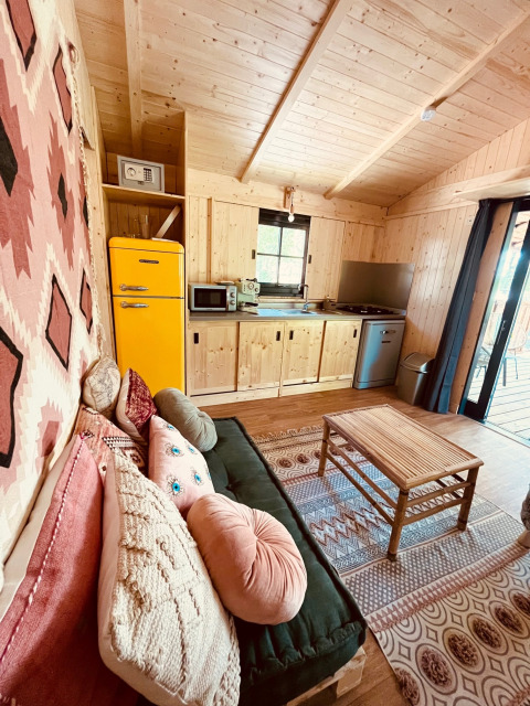 Cabane de glamping chaleureuse au Whaka Lodge avec intérieur en bois, déco colorée, cuisine et salon confortable.