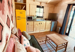 Gemütliche Glamping-Unterkunft mit Holzverkleidung, bunter Dekoration, Sofa und Küche bei Whaka Lodge.