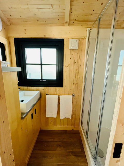 Salle de bains moderne à Whaka Lodge glamping avec murs en bois, fenêtre, lavabo et cabine de douche.