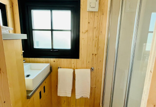 Modern bathroom at Whaka Lodge glamping with wooden walls, black-framed window, sink and shower cabin.