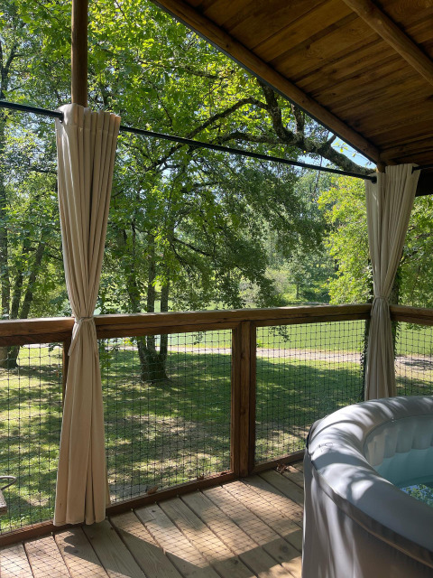 View from Whaka Lodge glamping deck in South France, showing trees, curtains, railing and hot tub.