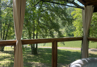View from Whaka Lodge glamping deck in South France, showing trees, curtains, railing and hot tub.