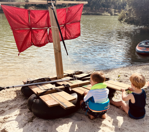 Dos niños juegan junto a una balsa artesanal con vela roja en la arena en Whaka Lodge en el sur de Francia.