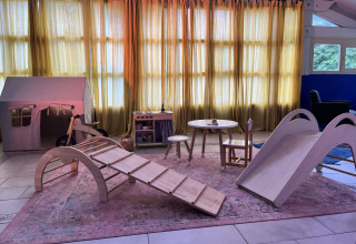 Innenraum-Spielbereich in Whaka Lodge Glamping mit Holzspielzeug, Rutsche und Kindertisch vor Vorhängen.