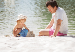 Ein Mann und ein Kind bauen eine Sandburg am See bei Whaka Lodge Glamping in Südfrankreich.