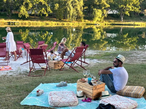 Folk nyder afslapning ved en sø på Whaka Lodge glamping i Sydfrankrig med stole, tæpper og snacks.