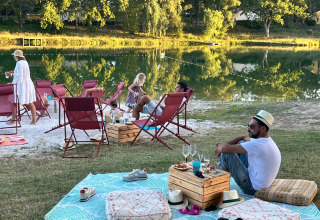Folk nyder afslapning ved en sø på Whaka Lodge glamping i Sydfrankrig med stole, tæpper og snacks.