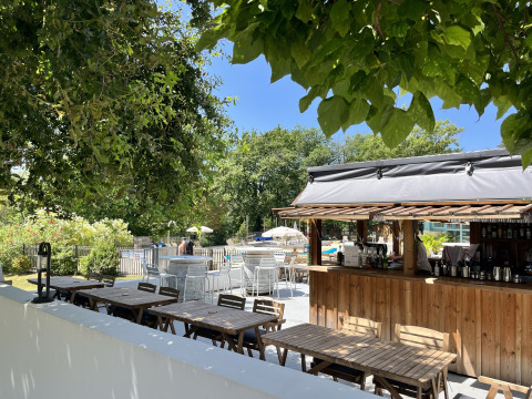 Udendørs caféområde med træborde, bar og swimmingpool på Whaka Lodge - Glamping i Sydfrankrig.